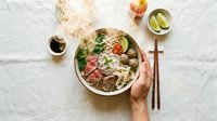Asian noodle soup bowl with fresh vegetables and meat, held by hand over white linen background. Flat lay food photography for culinary and restaurant design.