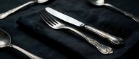 Elegant silverware set with fork and knife arranged on dark linen napkin, formal dining table setting for restaurant, catering, hospitality and event planning design projects.