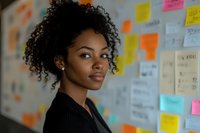 Young African American businesswoman with natural curly hair smiling confidently in office setting with colorful sticky notes and planning board in background.