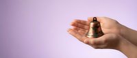 Hands holding small bronze bell on purple gradient background for meditation, mindfulness practice, spiritual wellness and relaxation concepts.