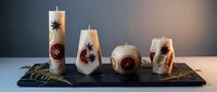 Decorative candles with dried flowers and botanicals embedded in wax, arranged on a dark slate tray with feather accents for home decor and aromatherapy styling.