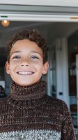 Cheerful mixed-race boy with freckles wearing brown turtleneck sweater smiling brightly at camera. Close-up portrait showing natural joy and innocence.