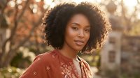 Young African American woman with curly afro hair in rust embroidered top during golden hour sunset light for lifestyle and beauty content.