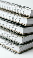 Stack of spiral-bound notebooks with metal wire binding, stacked on white background, for education, office, and stationery supply concepts.