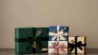 Wrapped gift boxes in green, blue, cream and natural kraft paper with decorative ribbons and bows arranged on wooden surface for holiday, celebration and special occasion designs.