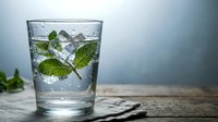 Refreshing glass of water with fresh mint leaves and ice cubes on rustic wooden table for healthy hydration and wellness lifestyle concepts.