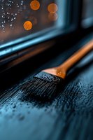 Paint brush with black bristles on dark wooden surface with orange bokeh lights in background, creating moody artistic atmosphere for renovation projects.