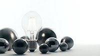 Illuminated vintage filament light bulb surrounded by dark spheres on white surface, representing innovation and creative ideas.