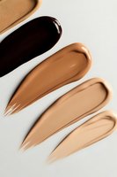 Liquid foundation swatches in different skin tone shades from dark to light on white background, showing texture and consistency of makeup product.