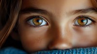 Close up portrait showing bright amber eyes and freckles against dark blue knitted fabric, creating dramatic lighting and intimate emotional atmosphere.