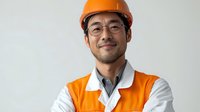 Asian male construction engineer wearing orange safety vest and hardhat smiling confidently with arms crossed against white background, professional portrait.