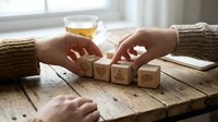 Hands arranging wooden letter blocks spelling LOVE on rustic table with tea cup in cozy home setting for relationship and romance concepts.