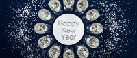 Happy New Year greeting card with champagne glasses arranged in a circle on dark blue background with silver glitter and stars.