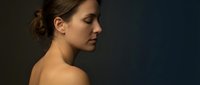 Young Caucasian woman in profile with bare shoulders against dark blue background, serene expression and natural makeup for beauty and wellness concepts.