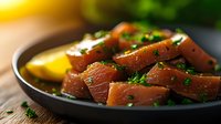 Fresh raw salmon fillet pieces seasoned with herbs, black pepper and chives on dark plate with lemon slice, close up view of gourmet seafood preparation.
