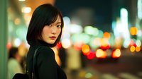 Young Asian woman with short black hair looking over shoulder at night in urban city with blurred colorful lights and bokeh background creating atmospheric mood.