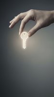 Hand holding glowing neon key against gray background, symbolizing access, security, and opportunity for real estate, business, and technology concepts.