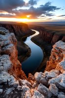 Dramatic sunset illuminates winding river canyon with golden light casting shadows on steep rock walls while clouds break over distant horizon at dusk.