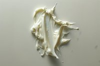 Elegant white cream swirl floating against neutral background, soft flowing texture with peaks and folds creates dynamic movement and luxurious appearance.