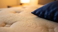 Close-up of beige textured bedding with navy blue pillow, warm ambient lighting creating cozy bedroom atmosphere for home decor and interior design projects.
