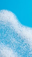 White foam bubbles on bright blue water surface creating abstract cleaning and freshness concept for hygiene products and spa treatments.