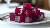 Vibrant purple beetroot jelly cubes arranged on white plate, showcasing glossy texture and rich color for culinary photography or food blog content.