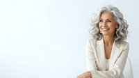 Mature woman with gray wavy hair wearing cream blazer, smiling confidently against white background. Suitable for business, corporate, healthcare, and lifestyle marketing materials.