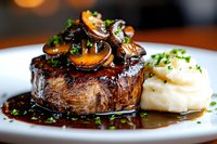 Juicy grilled beef tenderloin steak topped with sauteed mushrooms and fresh herbs, served with creamy mashed potatoes in rich brown sauce on white plate.