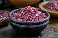 Pink Himalayan salt crystals in rustic black stone bowl on wooden surface, macro food photography showing mineral texture and natural color variation.