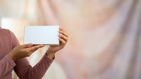 Person with medium skin tone holding blank white card or certificate in both hands, wearing mauve long-sleeved top. Suitable for business, education, and promotional materials.