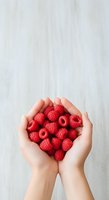 Hands holding fresh red raspberries arranged in heart shape against white wooden background. Isolated on white for design, packaging, and culinary projects.