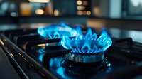 Blue gas flame burning on modern kitchen stove burner, close-up view showing energy consumption and cooking preparation in dark atmosphere.