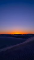 Desert sand dunes at sunset with golden orange sky transitioning to deep blue, creating dramatic landscape for travel and nature backgrounds.