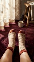 Cozy knitted wool socks on feet with coffee mug in warm home interior. Comfortable relaxation and hygge lifestyle concept for cold weather comfort.