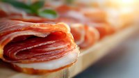 Thinly sliced prosciutto and mozzarella appetizer on wooden board with fresh herbs, macro shot showing delicate meat texture and layers in natural light.