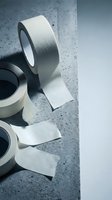 Silver metallic duct tape rolls on concrete surface with torn pieces, industrial adhesive material for construction and repair projects.