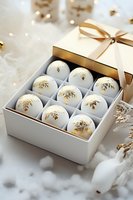 Elegant white and gold Christmas baubles with snowflake pattern arranged in gift box with satin ribbon on light festive background with bokeh lights and decorations.
