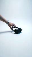 Hand with watch reaching for black wireless headphones on white background, music and technology concept.