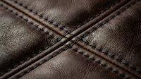 Brown leather surface with decorative cross-stitched seams showing detailed craftsmanship and texture for luxury goods and fashion accessories design.