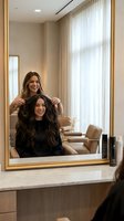 Professional hairstylist styling young woman's long brown hair in modern luxury salon with mirror reflection and natural lighting.