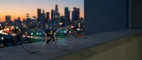 Eyeglasses on concrete ledge with blurred city skyline at sunset, vision correction concept for urban lifestyle and clear sight in metropolitan environment.