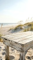 Weathered wooden table on sandy beach with dunes and sea oats in background, coastal seascape setting for travel, vacation, and outdoor lifestyle design projects.