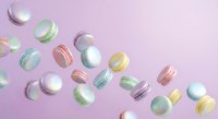Colorful macarons scattered on soft pink background creating sweet dessert pattern for bakery and confectionery designs.