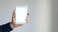 Hand holding tablet with blank white screen against neutral background, suitable for app mockups, technology presentations, and digital marketing materials.