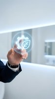 Businessman in dark suit touching glowing holographic icon combining gear and leaf symbols, representing sustainable technology and eco-friendly innovation in modern corporate environment.