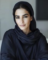 Middle Eastern woman wearing traditional black hijab and abaya smiling gently at camera against light background, showcasing modern modest fashion and natural makeup.