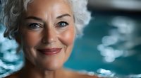 Smiling mature woman with silver hair and natural makeup enjoying wellness spa treatment near swimming pool with turquoise water reflections.