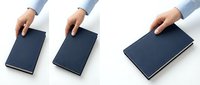 Hand of a young Caucasian person placing a dark navy blue hardcover book on a white surface, two angle views, clean minimal style.