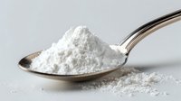 Fine white powder on silver spoon against light gray background, used in cooking, baking, pharmaceutical or cosmetic industry applications.