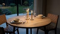 Elegant round wooden dining table set with candles, place settings, and modern chairs by illuminated garden at dusk for entertaining and home decor.